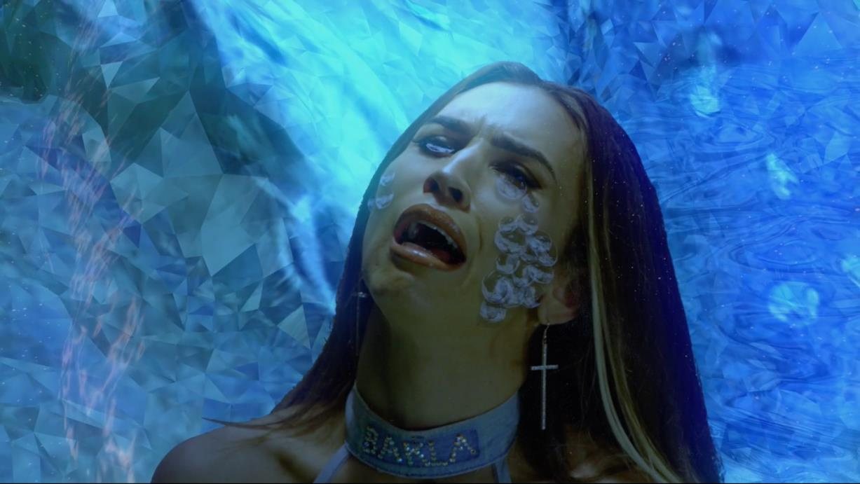 Still from Ex Nilalang: figure with glass tears against blue crystalline light