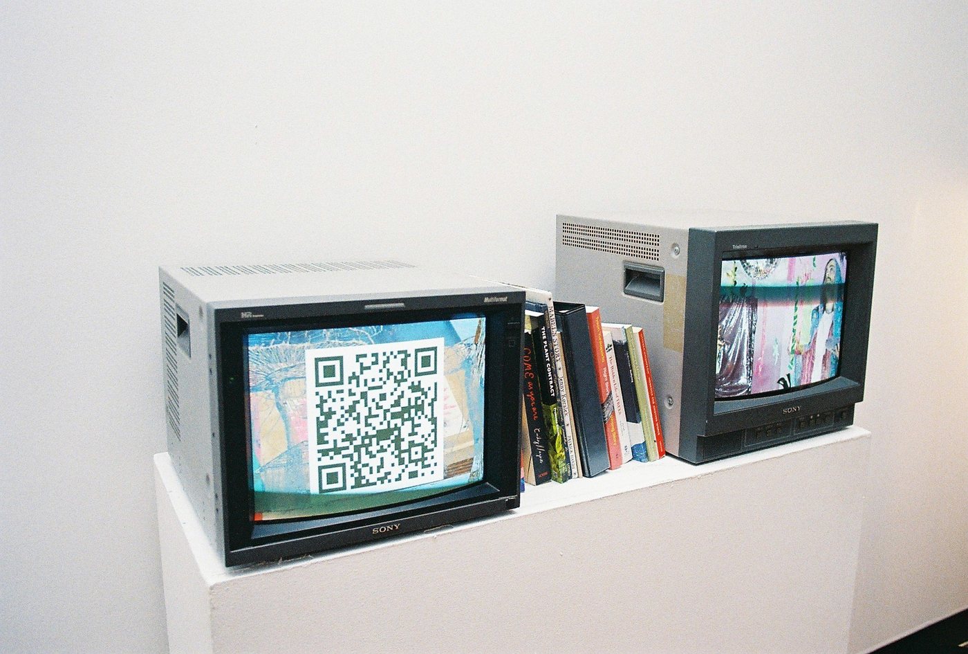 CRT monitors showing QR codes beside a row of books